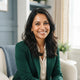 A smiling South Asian woman with glowing, healthy skin, captured in a professional headshot against a soft-focus, modern back